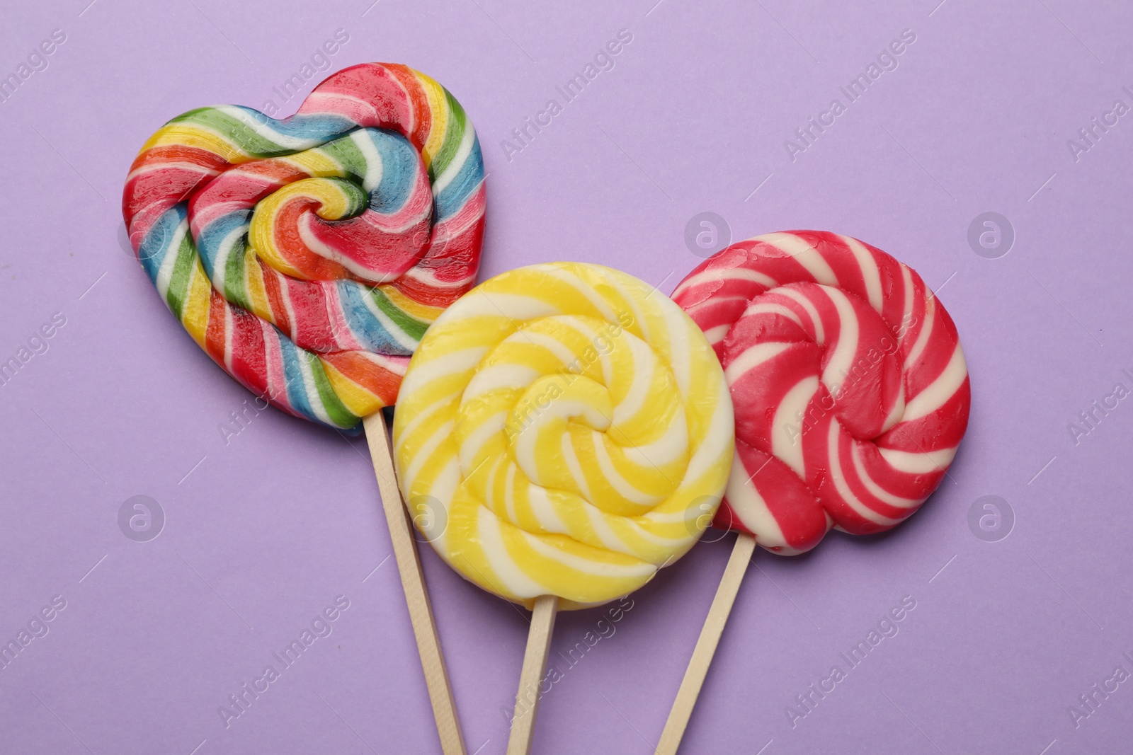 Photo of Tasty lollipops on violet background, flat lay