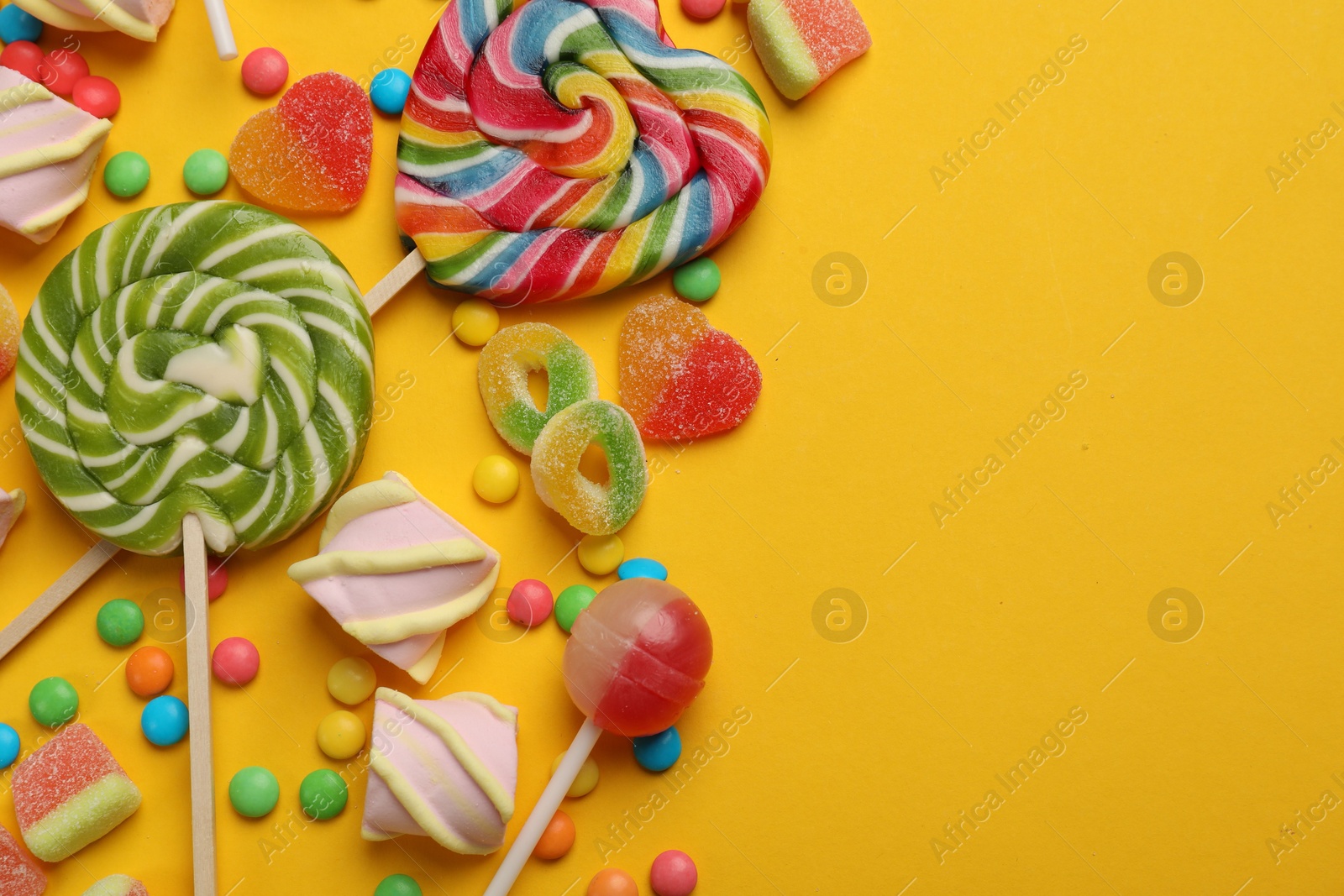 Photo of Many different tasty candies and marshmallows on yellow background, flat lay. Space for text