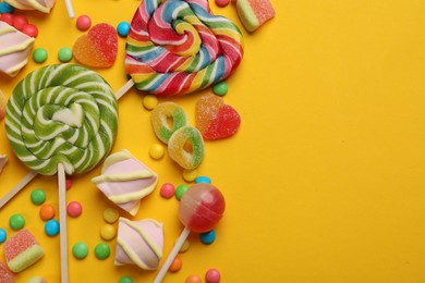 Photo of Many different tasty candies and marshmallows on yellow background, flat lay. Space for text