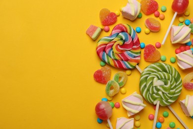 Photo of Many different tasty candies and marshmallows on yellow background, flat lay. Space for text