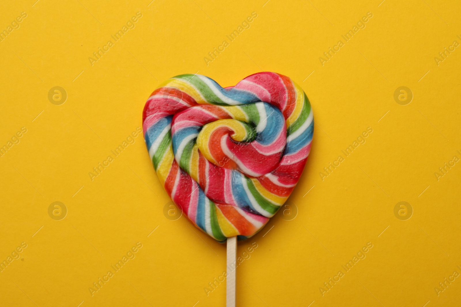 Photo of Tasty heart shaped lollipop on yellow background, top view