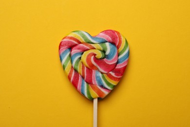 Tasty heart shaped lollipop on yellow background, top view