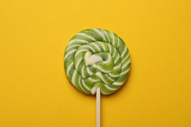 Photo of Tasty striped lollipop on yellow background, top view