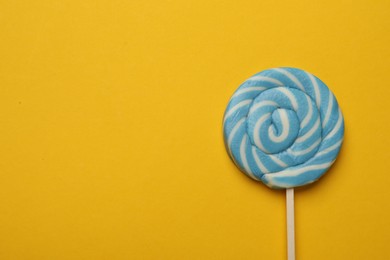 Photo of Tasty striped lollipop on yellow background, top view. Space for text