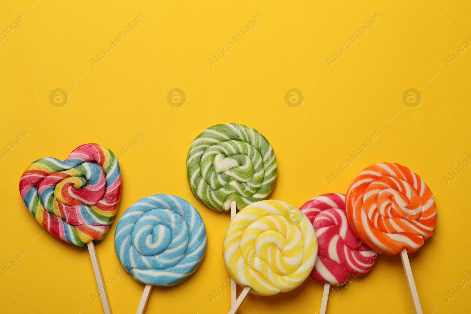 Photo of Tasty lollipops on yellow background, flat lay. Space for text