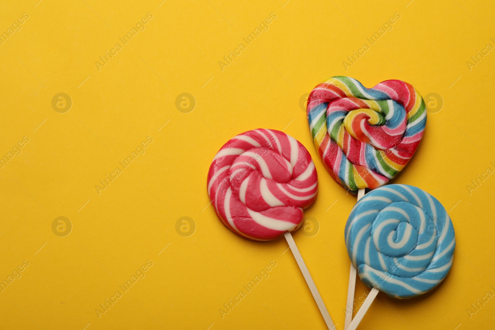 Photo of Tasty lollipops on yellow background, flat lay. Space for text