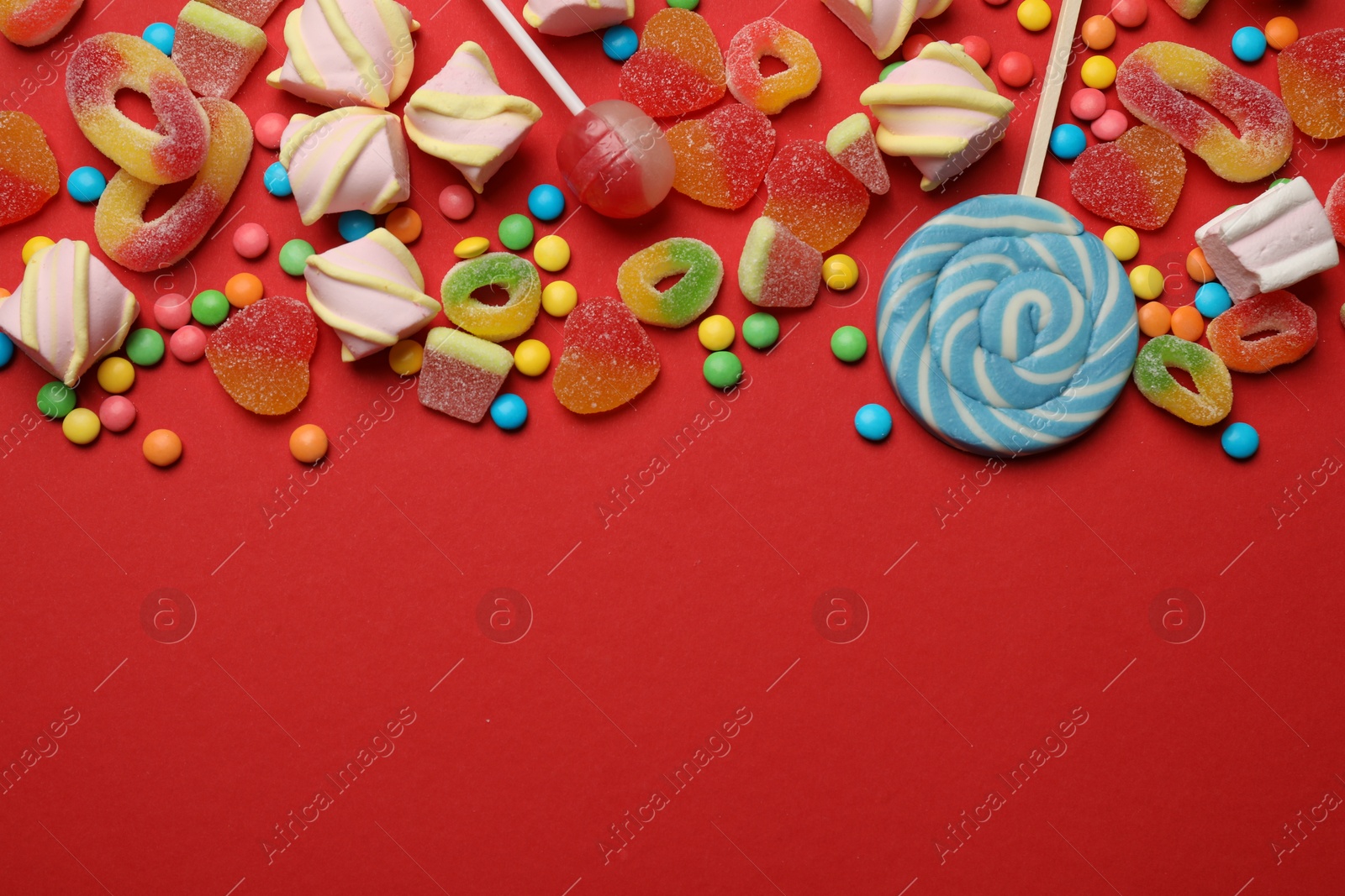 Photo of Many different tasty candies and marshmallows on red background, flat lay. Space for text