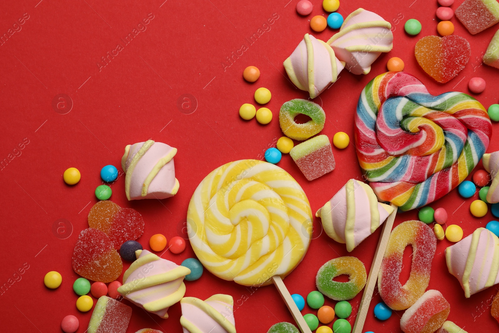 Photo of Many different tasty candies and marshmallows on red background, flat lay