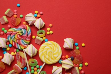 Photo of Many different tasty candies and marshmallows on red background, flat lay. Space for text