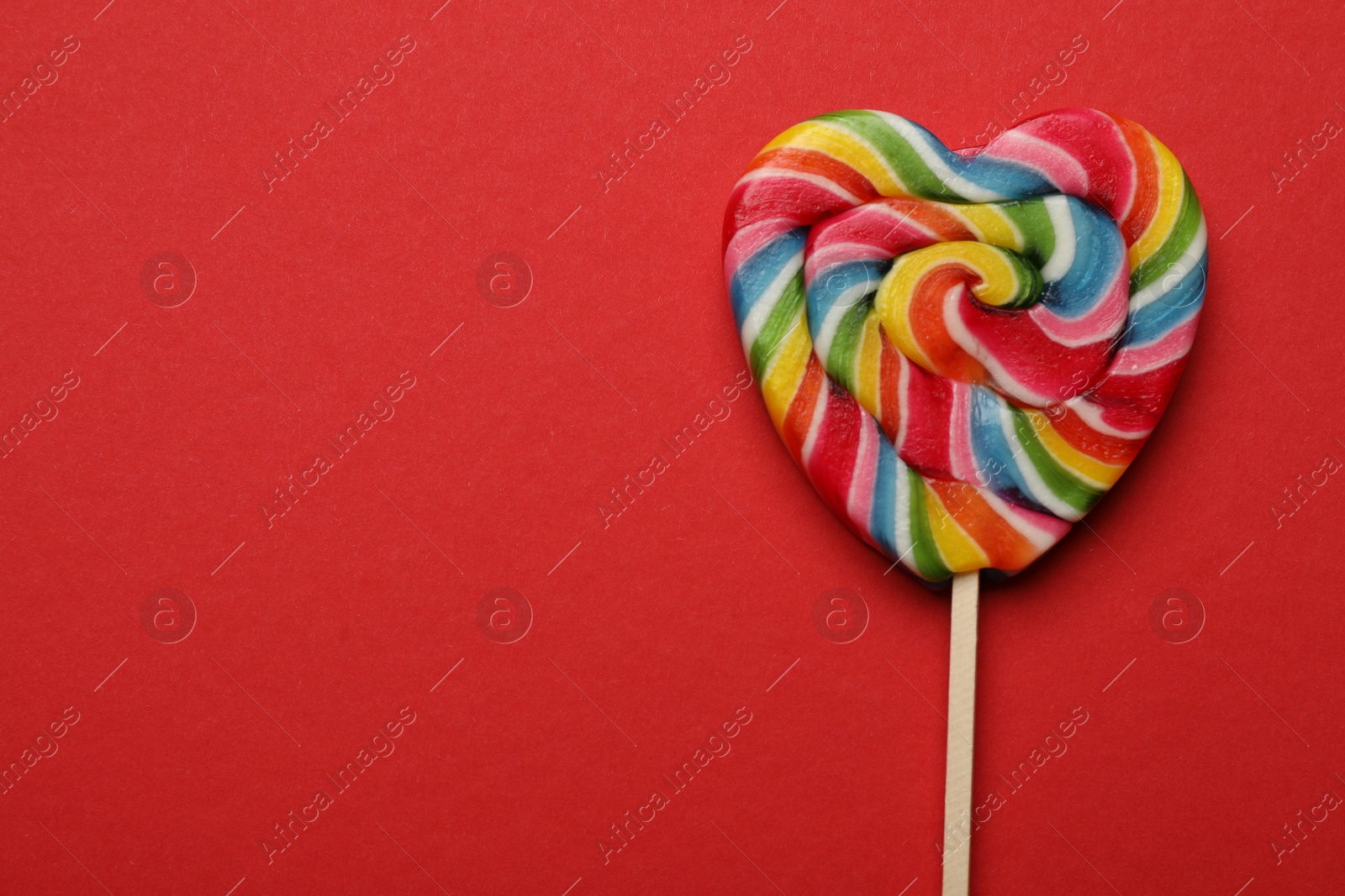 Photo of Tasty heart shaped lollipop on red background, top view. Space for text