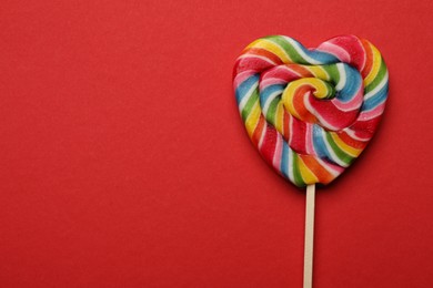 Photo of Tasty heart shaped lollipop on red background, top view. Space for text