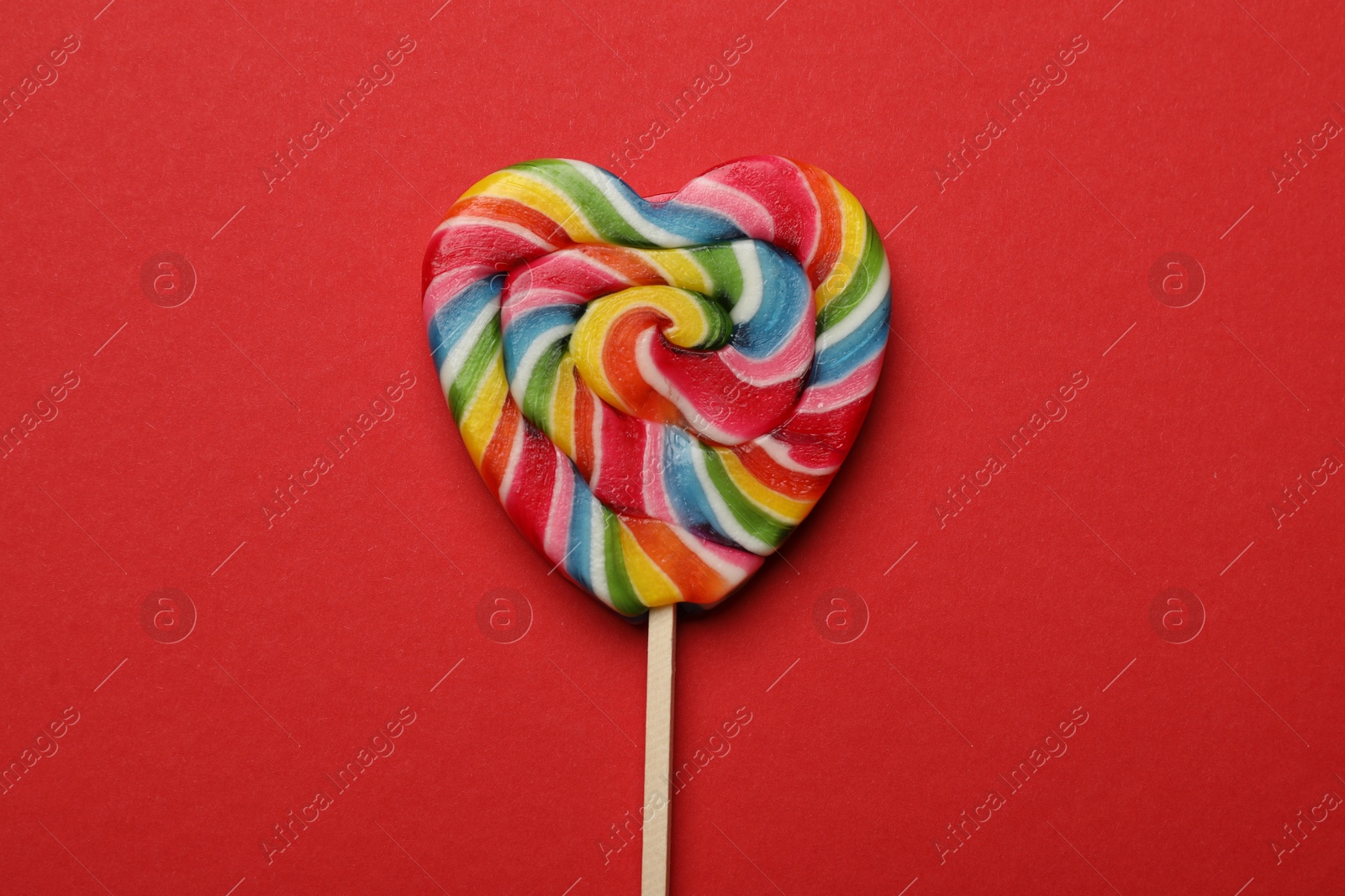 Photo of Tasty heart shaped lollipop on red background, top view