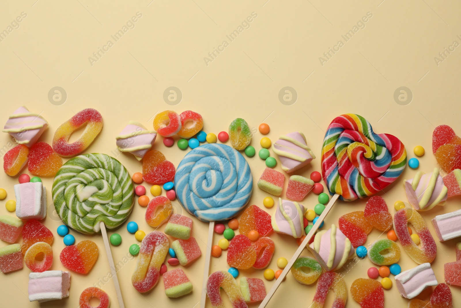 Photo of Many different tasty candies and marshmallows on beige background, flat lay. Space for text