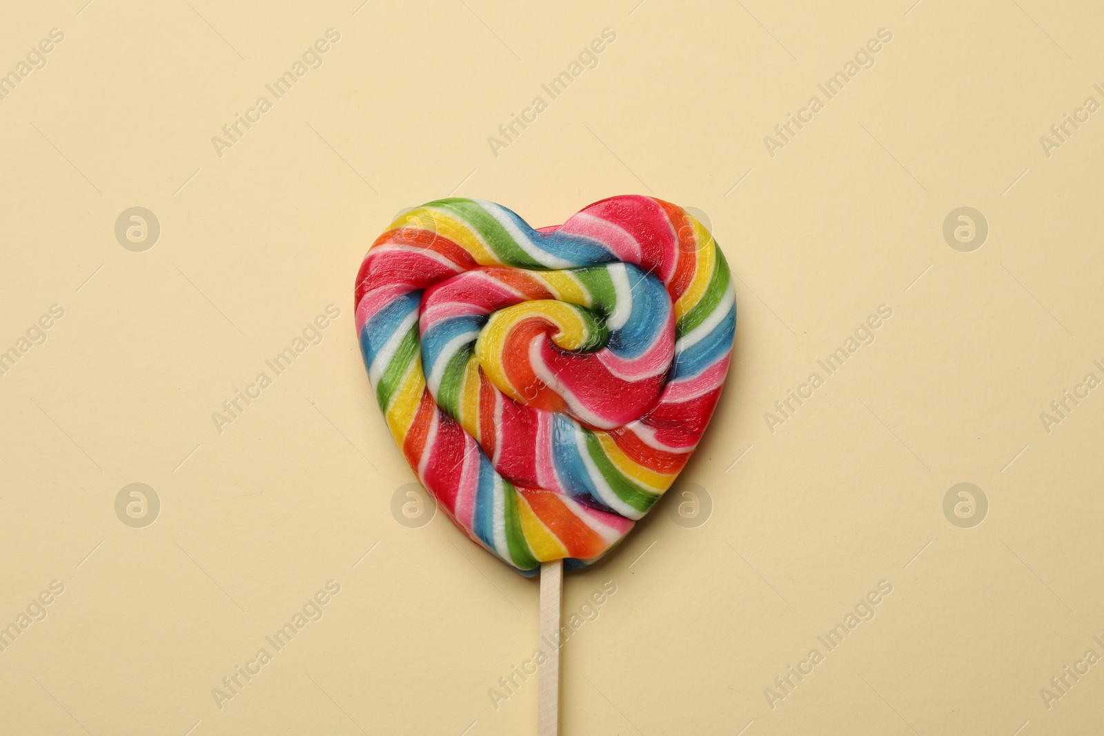 Photo of Tasty heart shaped lollipop on beige background, top view