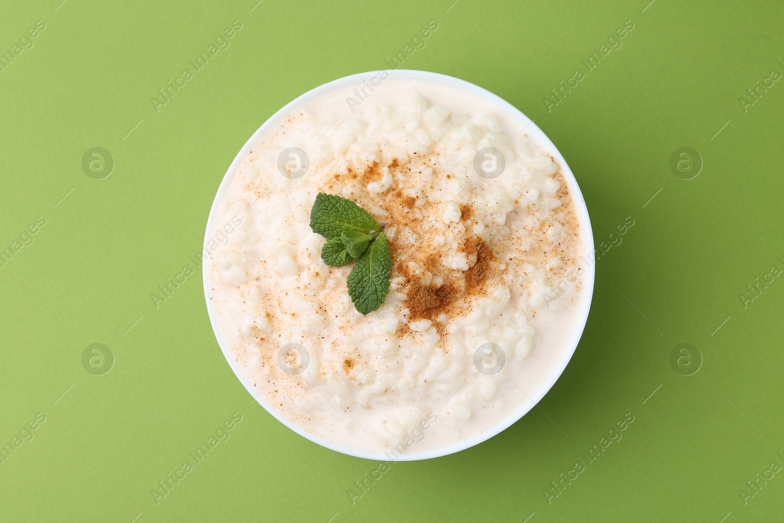 Photo of Tasty rice pudding with cinnamon and mint in bowl on green background, top view