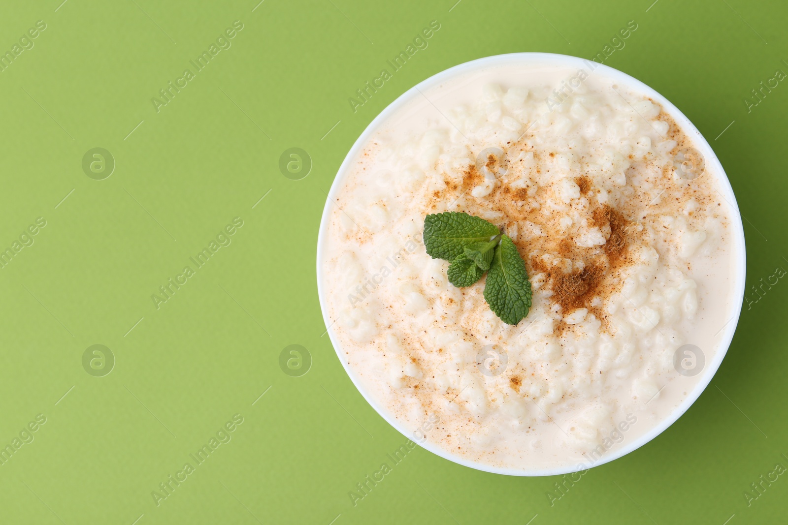 Photo of Tasty rice pudding with cinnamon and mint in bowl on green background, top view. Space for text