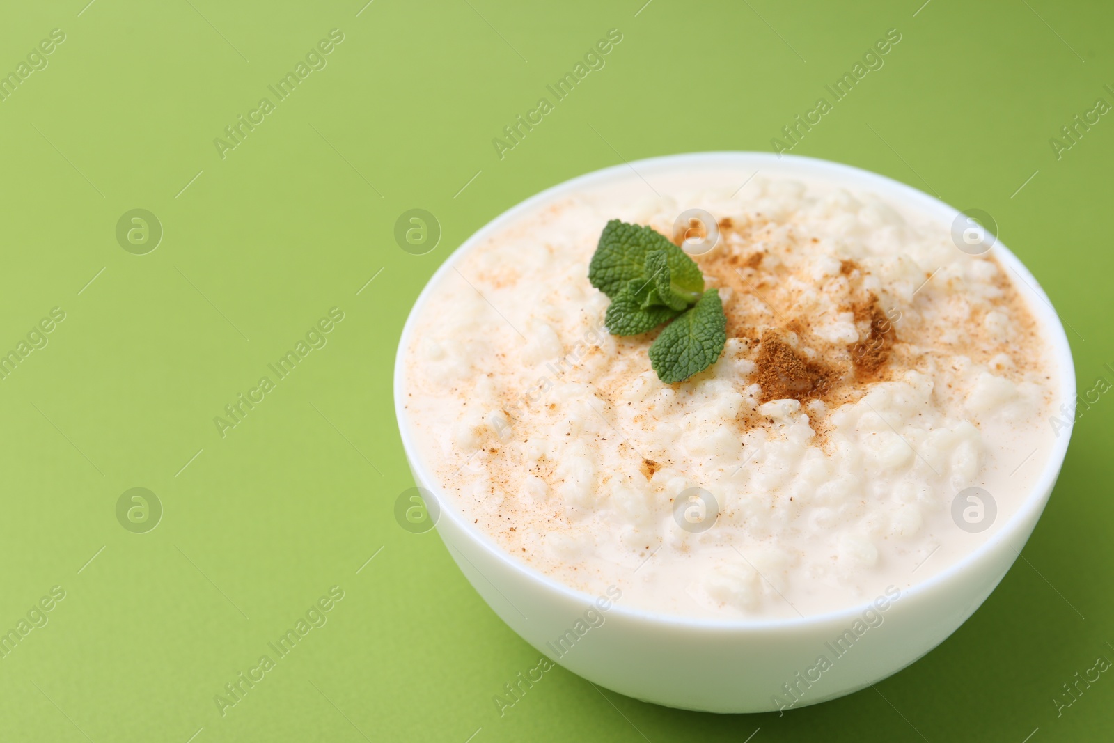 Photo of Tasty rice pudding with cinnamon and mint in bowl on green background, closeup. Space for text