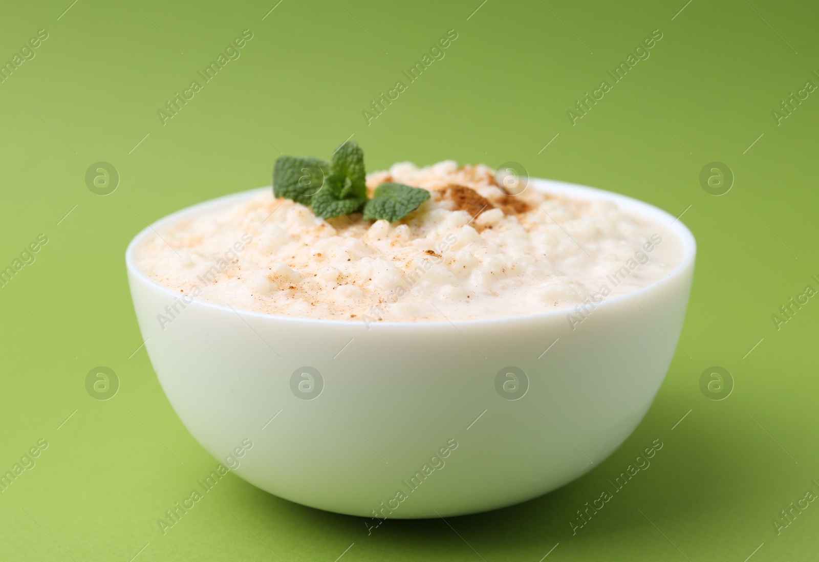 Photo of Tasty rice pudding with cinnamon and mint in bowl on green background, closeup