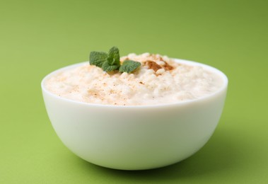 Photo of Tasty rice pudding with cinnamon and mint in bowl on green background, closeup