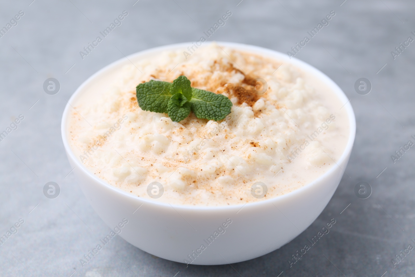 Photo of Tasty rice pudding with cinnamon and mint in bowl on grey table, closeup