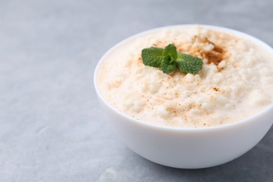 Photo of Tasty rice pudding with cinnamon and mint in bowl on grey table, closeup. Space for text