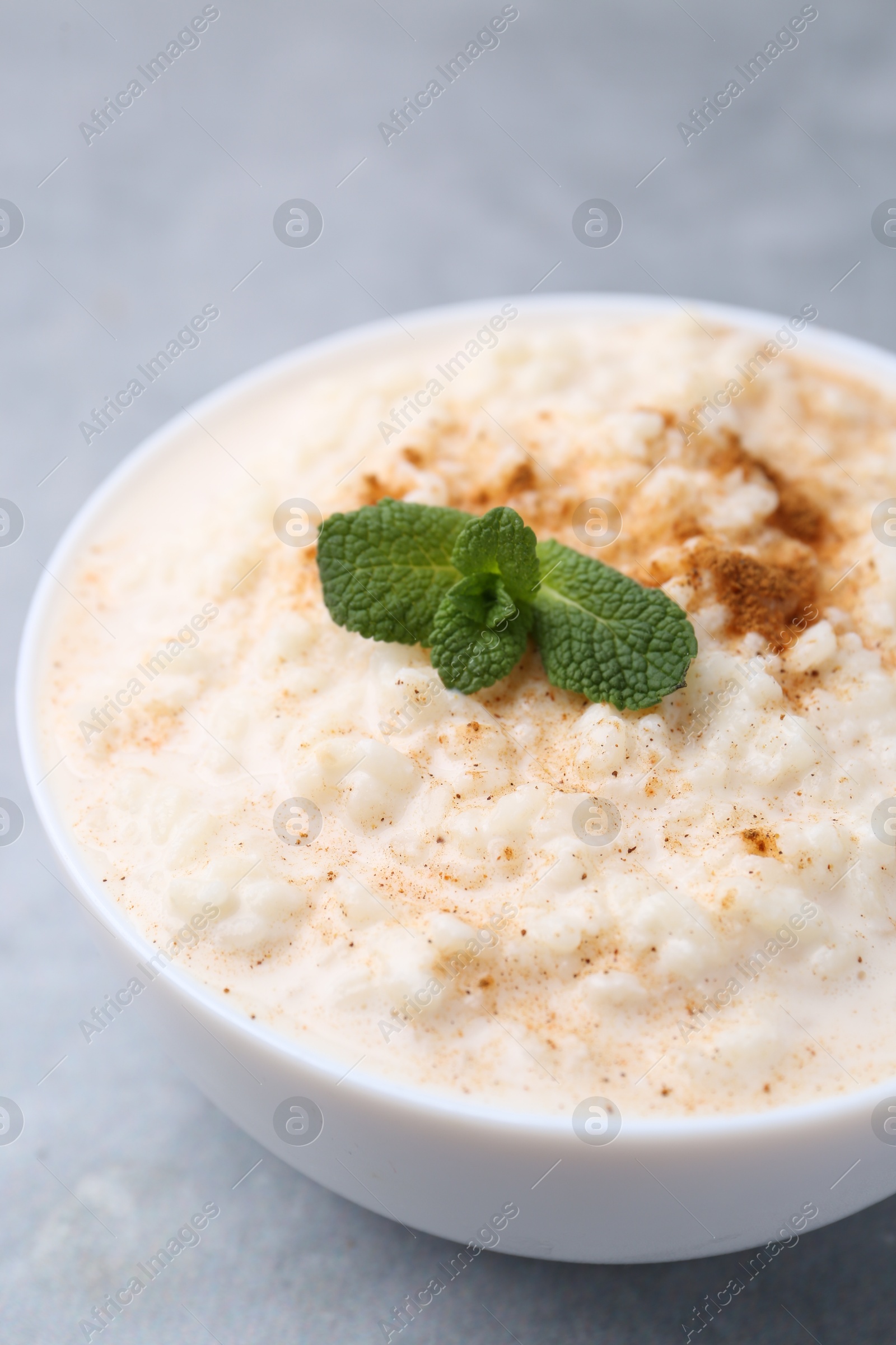 Photo of Tasty rice pudding with cinnamon and mint in bowl on grey table, closeup