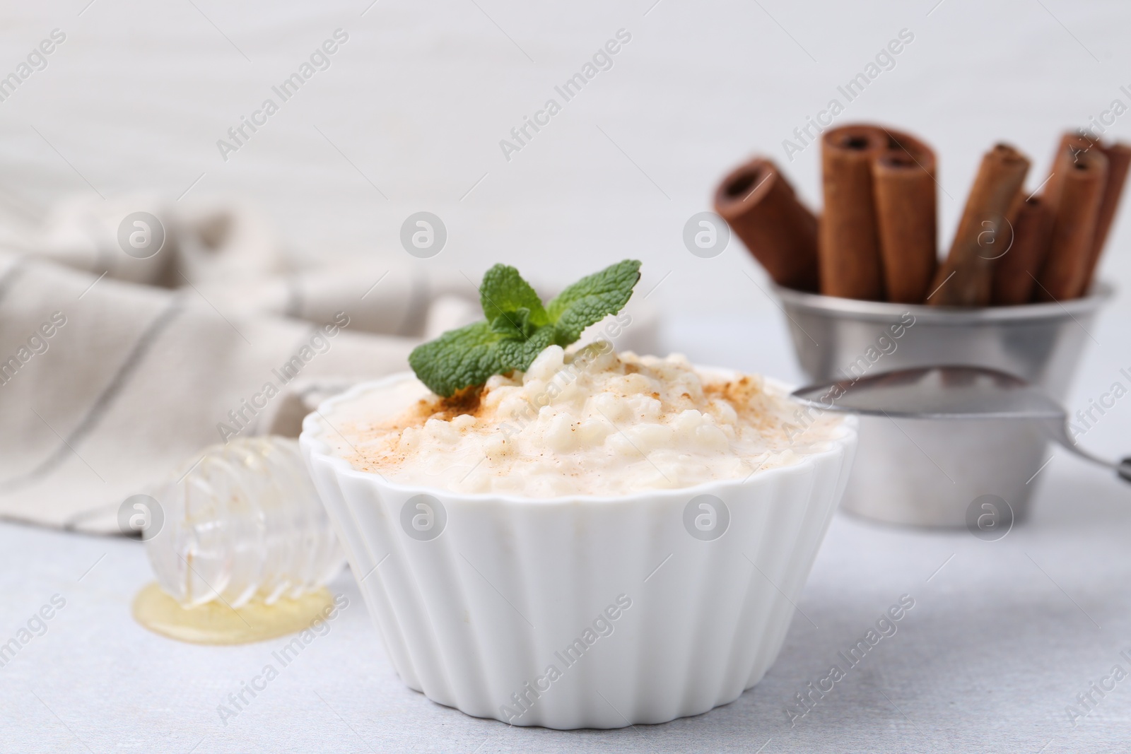 Photo of Tasty rice pudding with cinnamon and mint on light grey table, closeup