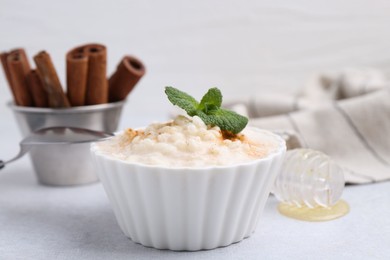 Photo of Tasty rice pudding with cinnamon and mint on light grey table, closeup