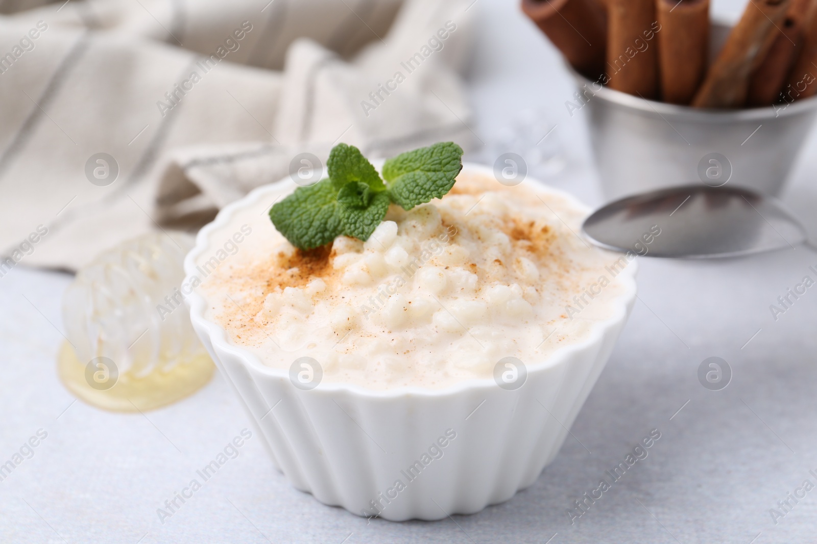 Photo of Tasty rice pudding with cinnamon and mint on light grey table, closeup