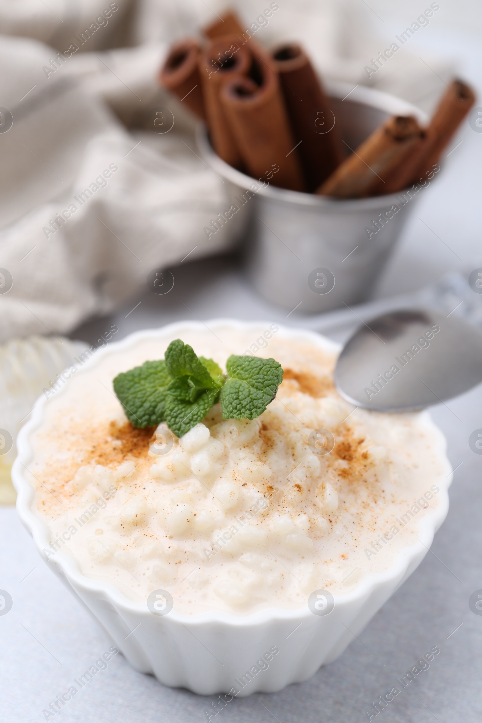 Photo of Tasty rice pudding with cinnamon and mint on light grey table, closeup