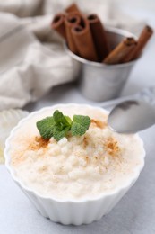 Photo of Tasty rice pudding with cinnamon and mint on light grey table, closeup