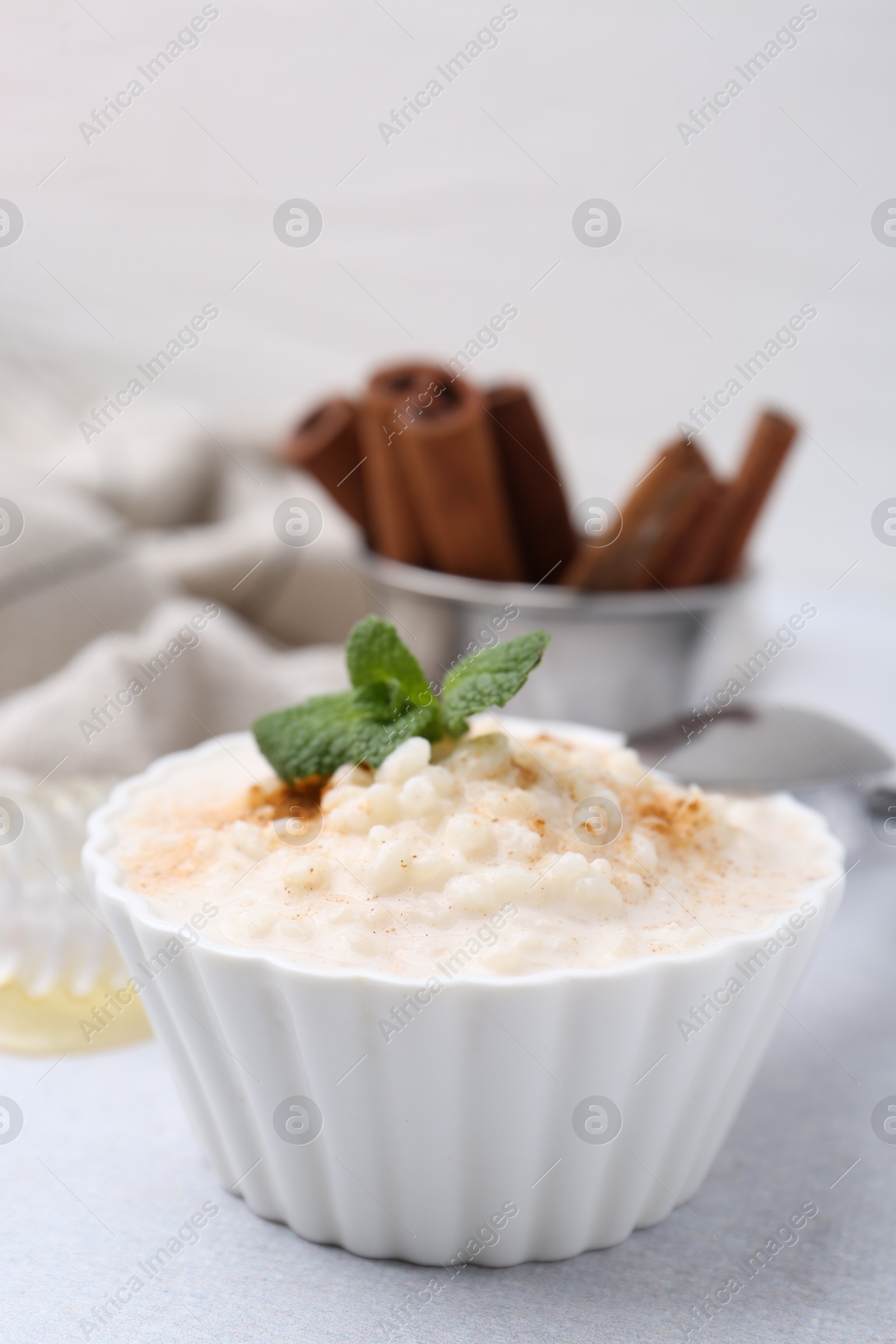 Photo of Tasty rice pudding with cinnamon and mint on light grey table, closeup