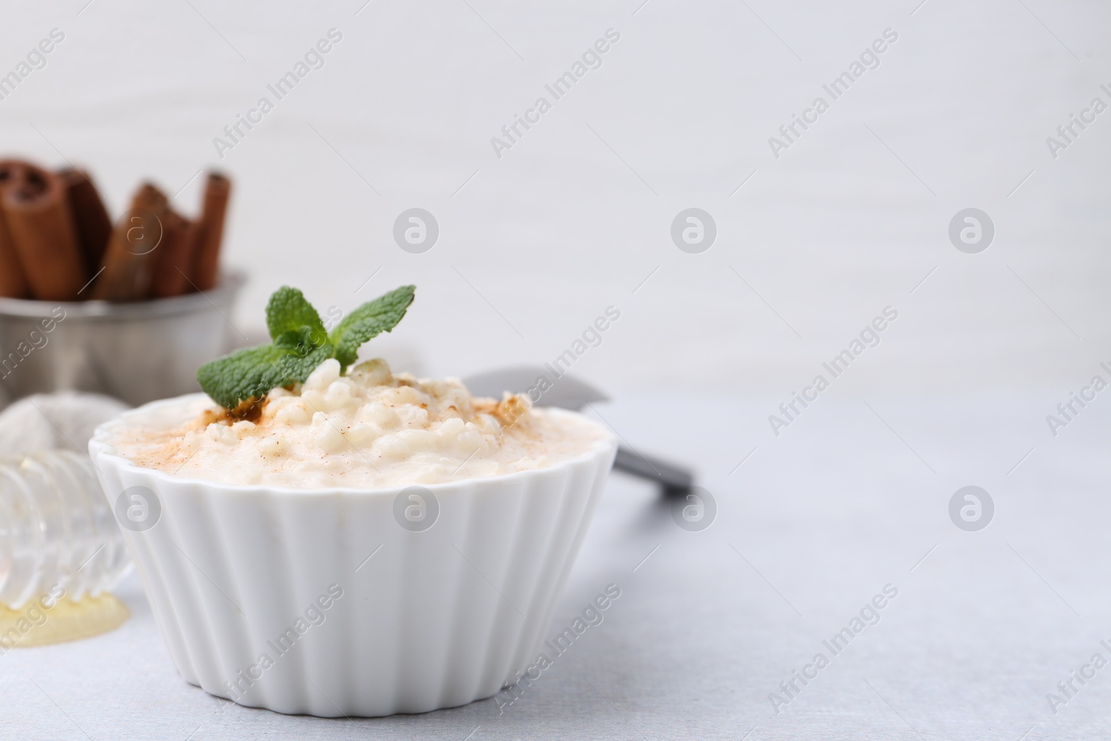 Photo of Tasty rice pudding with cinnamon and mint on light grey table, closeup. Space for text