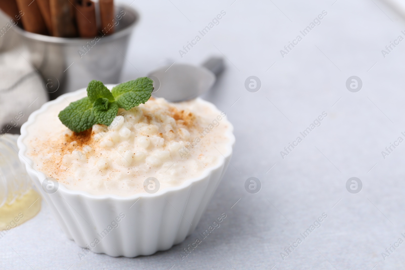 Photo of Tasty rice pudding with cinnamon and mint on light grey table, closeup. Space for text