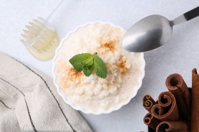 Photo of Tasty rice pudding with cinnamon and mint on light grey table, flat lay