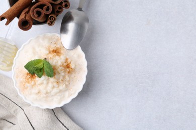 Photo of Tasty rice pudding with cinnamon and mint on light grey table, flat lay. Space for text