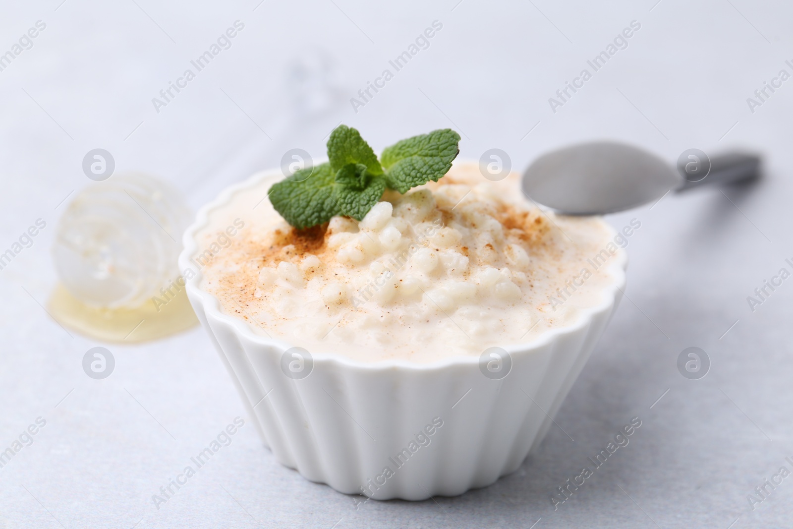 Photo of Tasty rice pudding with cinnamon and mint on light grey table, closeup