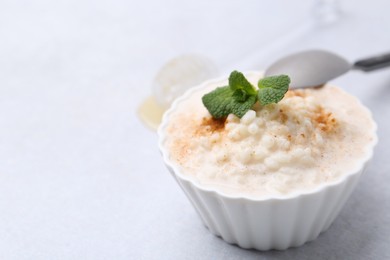 Photo of Tasty rice pudding with cinnamon and mint on light grey table, closeup. Space for text