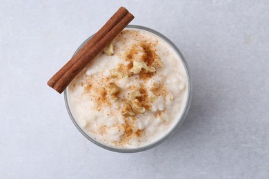 Photo of Tasty rice pudding with cinnamon and nuts in glass bowl on light grey table, top view