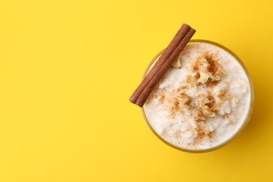 Photo of Tasty rice pudding with cinnamon and nuts in glass bowl on yellow background, top view. Space for text