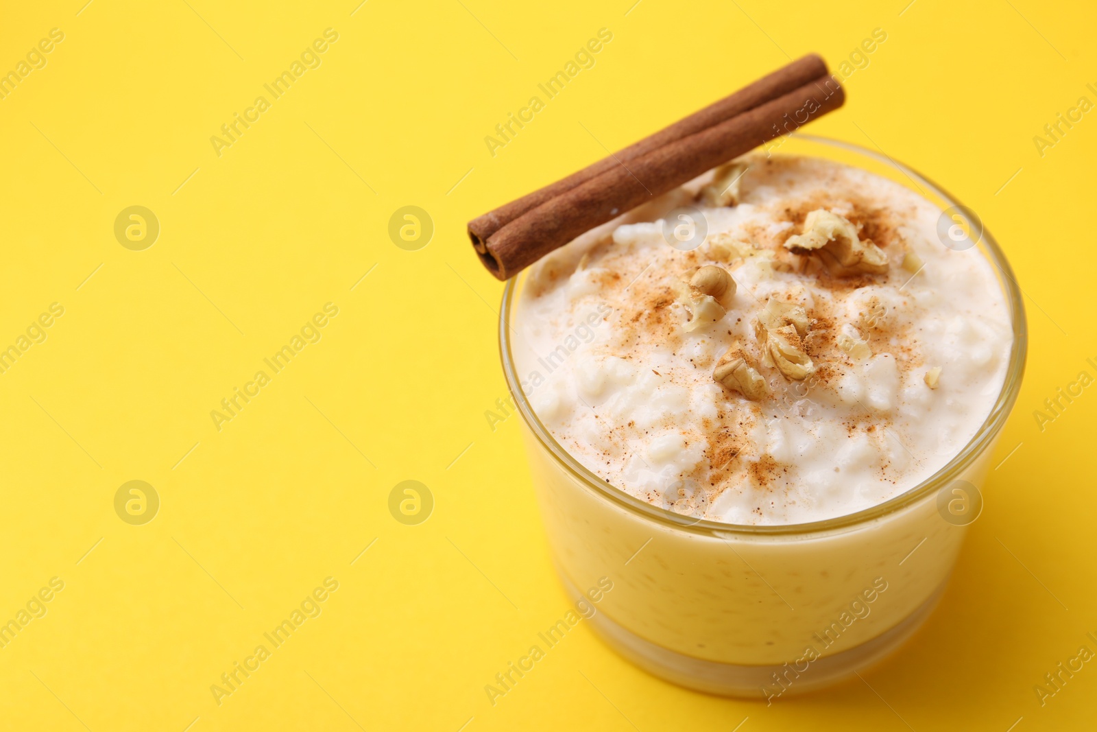 Photo of Tasty rice pudding with cinnamon and nuts in glass bowl on yellow background, closeup. Space for text