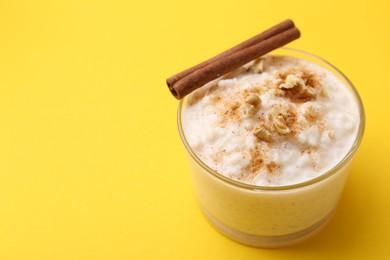 Photo of Tasty rice pudding with cinnamon and nuts in glass bowl on yellow background, closeup. Space for text