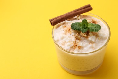 Photo of Tasty rice pudding with cinnamon, mint and nuts in glass bowl on yellow background, closeup. Space for text