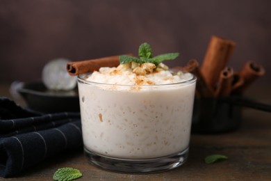 Photo of Tasty rice pudding with cinnamon, mint and nuts on wooden table, closeup