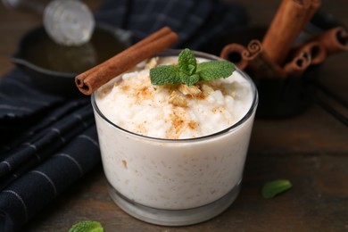 Photo of Tasty rice pudding with cinnamon, mint and nuts on wooden table, closeup