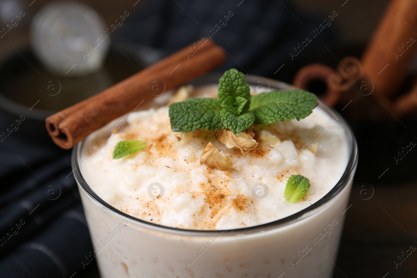 Photo of Tasty rice pudding with cinnamon, mint and nuts in glass bowl on table, closeup