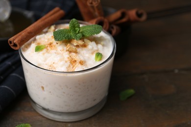 Photo of Tasty rice pudding with cinnamon, mint and nuts on wooden table, closeup. Space for text