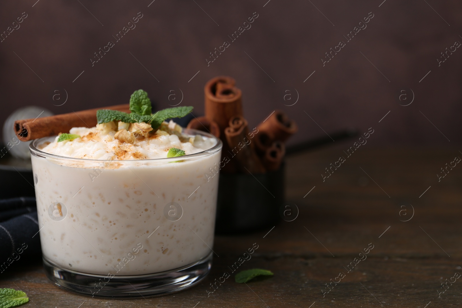 Photo of Tasty rice pudding with cinnamon, mint and nuts on wooden table, closeup. Space for text