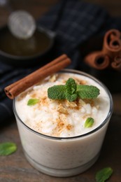 Photo of Tasty rice pudding with cinnamon, mint and nuts on wooden table