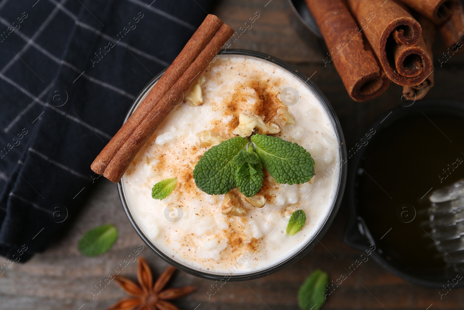 Photo of Tasty rice pudding with cinnamon, mint and nuts on wooden table, flat lay